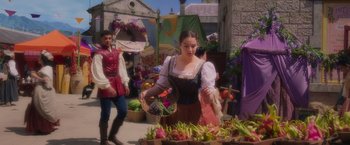 Movie still from “Disenchanted” (2022), directed by Adam Shankman – A woman in a medieval dress standing next to a table full of vegetables; Medium shot, Over the shoulder angle
