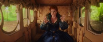 Movie still from “Disenchanted” (2022), directed by Adam Shankman – A woman sitting on top of a couch wearing a blue dress; Medium shot, Over the shoulder angle