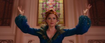 Movie still from “Disenchanted” (2022), directed by Adam Shankman – A woman in a peacock inspired outfit poses in front of a stained glass window; Medium shot, Low angle