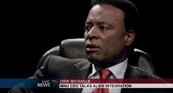 Movie still from “District 9” (2009), directed by Neill Blomkamp – A man in a suit and tie sitting in a chair; Close Up shot, Over the shoulder angle