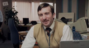 Movie still from “District 9” (2009), directed by Neill Blomkamp – A man sitting at a computer desk wearing headphones; Medium shot, Over the shoulder angle