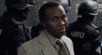 Movie still from “District 9” (2009), directed by Neill Blomkamp – A man in a suit and tie standing in front of a group of people; Close Up shot, Over the shoulder angle