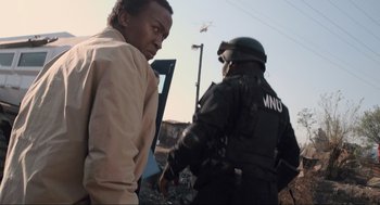 Movie still from “District 9” (2009), directed by Neill Blomkamp – A man in a tan shirt and a man in a black suit and helmet; Medium shot, Low angle