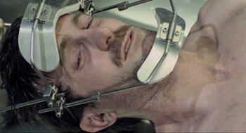 Movie still from “District 9” (2009), directed by Neill Blomkamp – A person wearing a metal head hammock; Close Up shot, Overhead angle