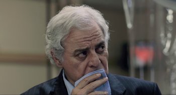 Movie still from “District 9” (2009), directed by Neill Blomkamp – An older man in a suit and tie holding his hand to his mouth; Close Up shot, Over the shoulder angle