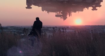 Movie still from “District 9” (2009), directed by Neill Blomkamp – A man sitting on top of a grass covered field; Extreme Wide shot, Over the shoulder angle