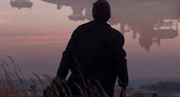 Movie still from “District 9” (2009), directed by Neill Blomkamp – A man standing on top of a grass covered field; Wide shot, Low angle