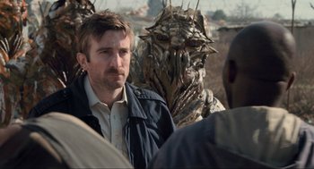 Movie still from “District 9” (2009), directed by Neill Blomkamp – A man standing in front of a group of people; Close Up shot, Over the shoulder angle