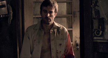 Movie still from “District 9” (2009), directed by Neill Blomkamp – A man with a bloody shirt on standing next to a door; Medium shot, Over the shoulder angle