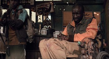 Movie still from “District 9” (2009), directed by Neill Blomkamp – A man sitting on a chair looking at his cell phone; Medium shot, Low angle