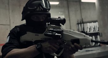 Movie still from “District 9” (2009), directed by Neill Blomkamp – A man in a black helmet holding a gun; Close Up shot, Over the shoulder angle