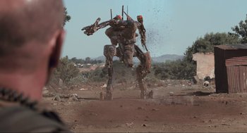 Movie still from “District 9” (2009), directed by Neill Blomkamp – An image of a robot in the middle of a dirt field; Wide shot, Over the shoulder angle
