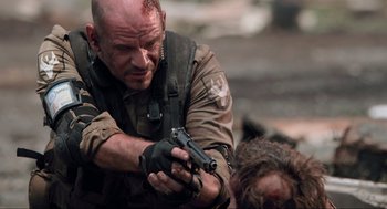 Movie still from “District 9” (2009), directed by Neill Blomkamp – A man with a gun in his hand and another man laying on the ground; Close Up shot, Over the shoulder angle