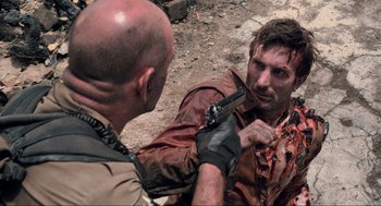Movie still from “District 9” (2009), directed by Neill Blomkamp – A man holding a gun in his hand while another man holds a knife in his other hand; Medium shot, Over the shoulder angle
