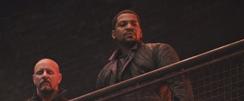 Movie still from “Divergent” (2014), directed by Neil Burger – A man standing next to a railing in the dark; Medium shot, Low angle