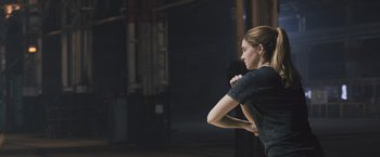 Movie still from “Divergent” (2014), directed by Neil Burger – A woman standing in a room holding her hands to her chest; Medium shot, Over the shoulder angle