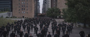 Movie still from “Divergent” (2014), directed by Neil Burger – A large group of men in black suits are marching down the street; Extreme Wide shot, High angle