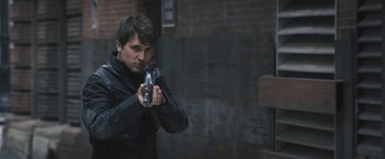 Movie still from “Divergent” (2014), directed by Neil Burger – A man in a black jacket holding a gun in his hand; Close Up shot, Low angle