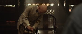 Movie still from “Doctor Strange” (2016), directed by Scott Derrickson – A bald man in a suit and tie holding a hammer; Medium shot, High angle