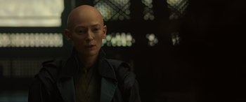 Movie still from “Doctor Strange” (2016), directed by Scott Derrickson – A woman with a bald head is standing in a dark room; Close Up shot, Over the shoulder angle