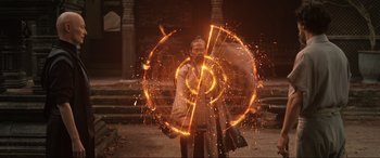 Movie still from “Doctor Strange” (2016), directed by Scott Derrickson – A man holding a sparkler in front of a building; Wide shot, High angle