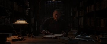 Movie still from “Doctor Strange” (2016), directed by Scott Derrickson – A man sitting at a table reading a book; Medium shot, Low angle