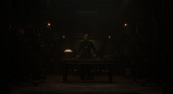 Movie still from “Doctor Strange” (2016), directed by Scott Derrickson – A man sitting at a table in a dark room; Wide shot, Low angle