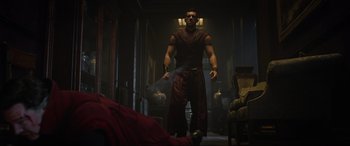 Movie still from “Doctor Strange” (2016), directed by Scott Derrickson – A man in a red shirt is standing in a room; Wide shot, Over the shoulder angle