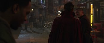 Movie still from “Doctor Strange” (2016), directed by Scott Derrickson – A man wearing a red cape standing on a city street; Medium shot, Over the shoulder angle