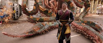 Movie still from “Doctor Strange in the Multiverse of Madness” (2022), directed by Sam Raimi – A man standing in front of a large dragon sculpture; Medium shot, Over the shoulder angle