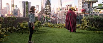 Movie still from “Doctor Strange in the Multiverse of Madness” (2022), directed by Sam Raimi – A woman in a red cape standing on a green lawn; Extreme Wide shot, Over the shoulder angle