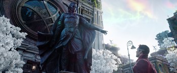 Movie still from “Doctor Strange in the Multiverse of Madness” (2022), directed by Sam Raimi – A large statue of a man and a woman in front of a clock tower; Extreme Wide shot, Low angle