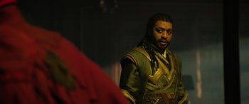 Movie still from “Doctor Strange in the Multiverse of Madness” (2022), directed by Sam Raimi – A man with long dreadlocks wearing a green and gold outfit; Medium shot, Over the shoulder angle