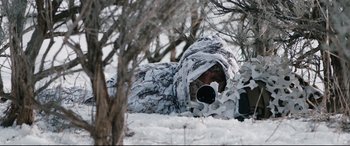 Movie still from “Wind River” (2017), directed by Taylor Sheridan – A man in a snow suit hiding in the snow; Medium shot, Over the shoulder angle