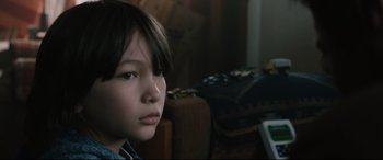 Movie still from “Wind River” (2017), directed by Taylor Sheridan – A young boy sitting on a couch looking at the camera; Close Up shot, Over the shoulder angle