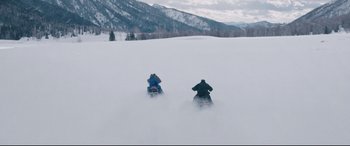 Movie still from “Wind River” (2017), directed by Taylor Sheridan – Two snowmobiles traveling down a snow covered slope; Extreme Wide shot, High angle