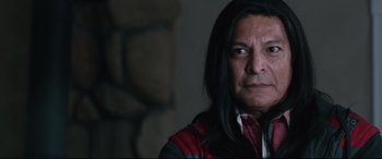 Movie still from “Wind River” (2017), directed by Taylor Sheridan – A man with long black hair wearing a red and black jacket; Close Up shot, Over the shoulder angle