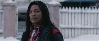 Movie still from “Wind River” (2017), directed by Taylor Sheridan – A man with long black hair wearing a red and black shirt; Close Up shot, Over the shoulder angle