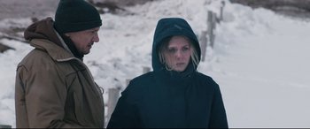 Movie still from “Wind River” (2017), directed by Taylor Sheridan – A woman wearing a hooded jacket and a man standing next to a fence; Medium shot, Over the shoulder angle