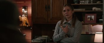 Movie still from “Wind River” (2017), directed by Taylor Sheridan – A young woman holding a wine glass while standing in a kitchen; Medium shot, Over the shoulder angle