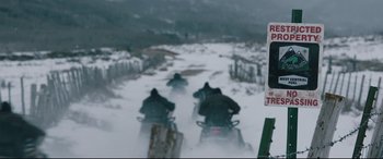 Movie still from “Wind River” (2017), directed by Taylor Sheridan – A group of people riding snowmobiles down a snow covered road; Wide shot, High angle