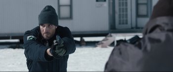 Movie still from “Wind River” (2017), directed by Taylor Sheridan – A man holding a handgun while standing in the snow; Medium shot, Over the shoulder angle
