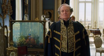 Movie still from “Dolittle” (2020), directed by Stephen Gaghan – An older man in a black and gold outfit; Medium shot, Over the shoulder angle