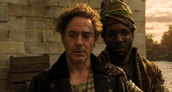 Movie still from “Dolittle” (2020), directed by Stephen Gaghan – A man and a woman standing next to a brick wall; Close Up shot, Over the shoulder angle