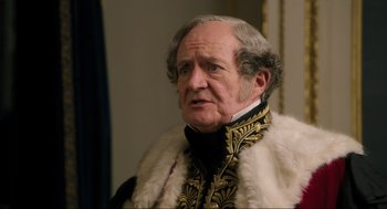 Movie still from “Dolittle” (2020), directed by Stephen Gaghan – An older man wearing a fur coat and a black and gold jacket; Close Up shot, Over the shoulder angle