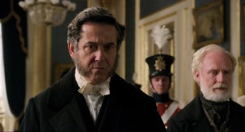 Movie still from “Dolittle” (2020), directed by Stephen Gaghan – A man in a suit and a hat standing in front of another man in a uniform; Close Up shot, Over the shoulder angle
