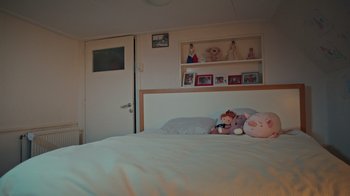Movie still from “Doll House” (2022), directed by Marla Ancheta – A child's bed with stuffed animals on it; Wide shot, High angle