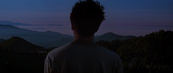 Movie still from “Donnie Darko” (2001), directed by Richard Kelly – A man standing in front of a view of mountains at night; Wide shot, Low angle