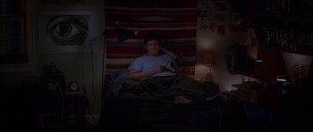 Movie still from “Donnie Darko” (2001), directed by Richard Kelly – A man sitting in a bed reading a book at night; Wide shot, High angle