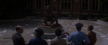 Movie still from “Donnie Darko” (2001), directed by Richard Kelly – A group of men standing around a statue of a bear; Wide shot, High angle